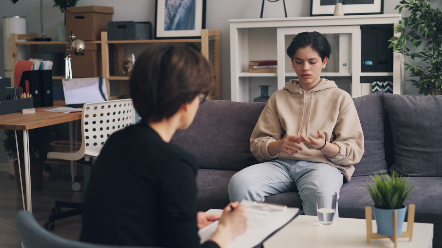 Professional counsels young person on a grey couch.